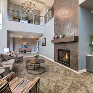 A modern living room with a high ceiling, featuring a cozy fireplace, stylish chandelier, and comfortable seating area.