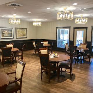 A cozy dining area featuring wooden tables and chairs, well-lit by elegant chandeliers.