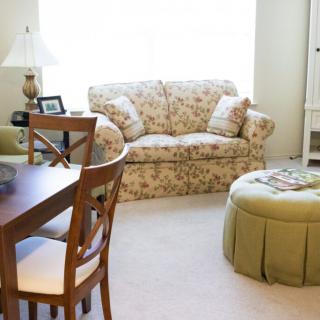 A cozy living room with a floral sofa, wooden dining table, and soft lighting.