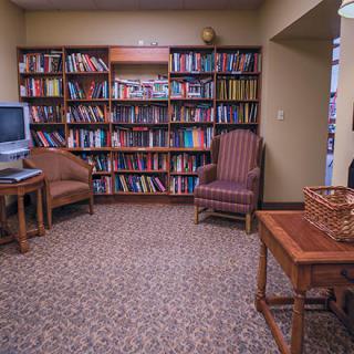 A cozy reading room with bookshelves, chairs, and a television.