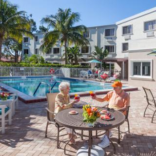 Two seniors enjoy a sunny day by the pool, savoring refreshments and good company.