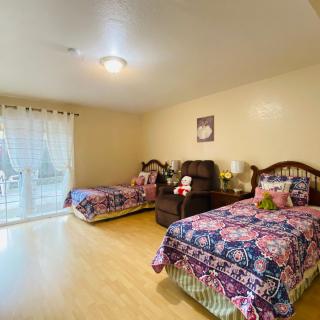 A cozy bedroom featuring two twin beds with floral bedspreads, an armchair, and a large window letting in natural light.