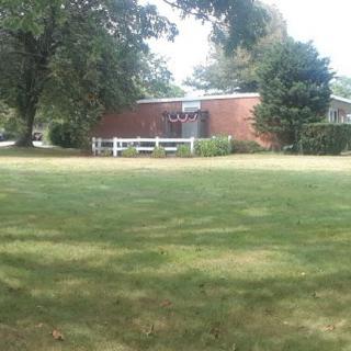A brick building surrounded by trees and a grassy field.