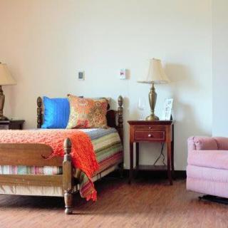 A cozy bedroom with a single bed, colorful pillows, and a side table with lamps.