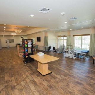 A spacious and bright rehabilitation therapy room with exercise equipment and wooden flooring.