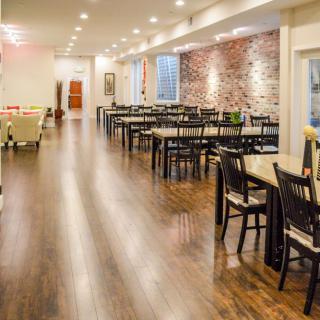 A spacious restaurant interior with neatly arranged tables and chairs, featuring a brick accent wall and wooden flooring.