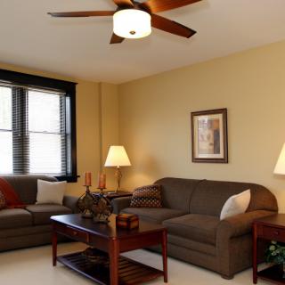 Cozy living room with brown sofas, a central coffee table, and a ceiling fan.