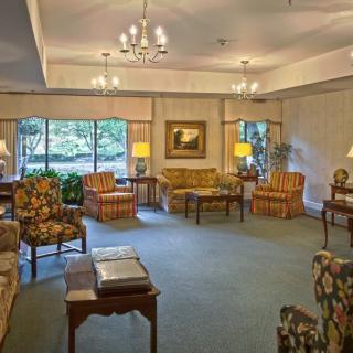 A cozy, traditionally decorated living room with multiple seating arrangements and large windows bringing in natural light.
