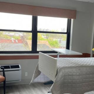 A hospital room with a single bed, large windows, and a chair.