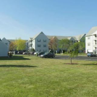 A suburban residential area with apartment buildings, green lawns, and a parking lot.