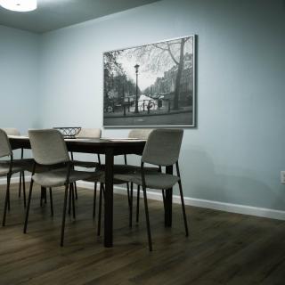 A minimalist dining room with a wooden table, chairs, and a framed artwork on the wall.