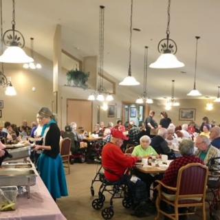 Elderly individuals enjoying a communal meal in a dining hall setting.