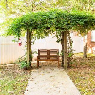 A serene garden bench under a vine-covered pergola along a concrete pathway.