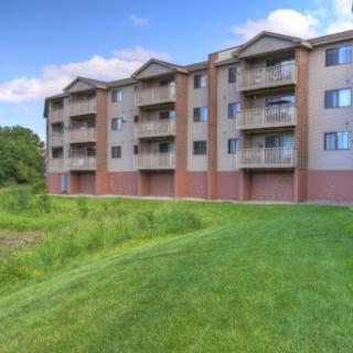 A modern apartment building with balconies set against a lush green landscape.