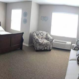 A cozy bedroom with a wooden bed, patterned armchair, and large windows letting in natural light.