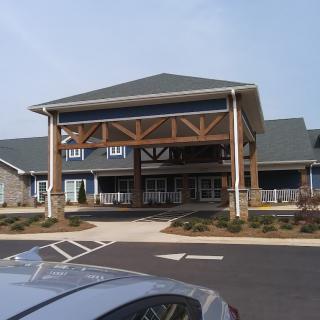 A modern building with a wooden-beamed entrance and a parking lot in the foreground.