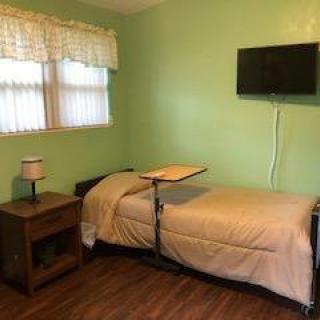 A simple bedroom with a single bed, nightstand, lamp, and wall-mounted television.
