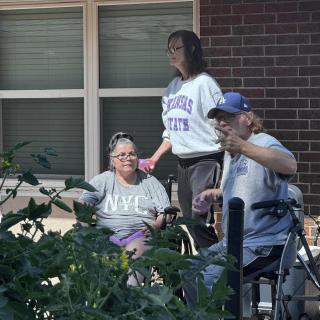 A group of people enjoying time outside in a garden setting, with two individuals in wheelchairs.