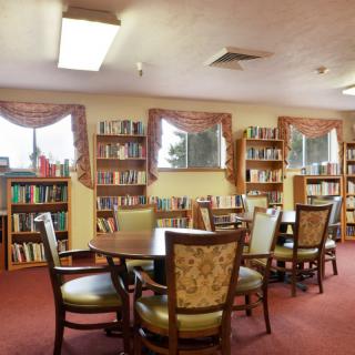 A cozy library room with bookshelves lining the walls and tables with chairs in the center.