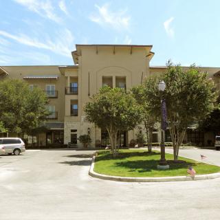 A sunny view of a hotel building with surrounding trees and a parking area.