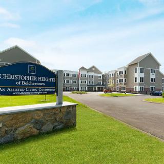 Exterior view of a senior living facility with a sign and landscaped grounds.
