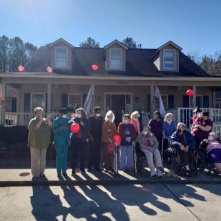 A group of people gathered outside a house, holding balloons on a sunny day.