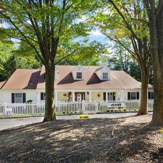 A charming suburban house surrounded by trees with a white fence.