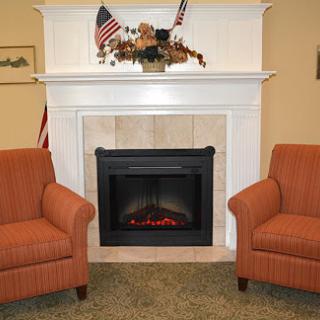 A cozy living room featuring an electric fireplace and two inviting orange armchairs.