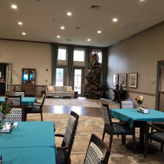 A well-decorated dining area with tables covered in teal tablecloths, featuring a large Christmas tree in the corner.