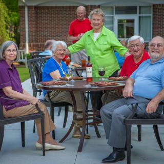 A group of seniors enjoying a gathering outdoors around a patio table.