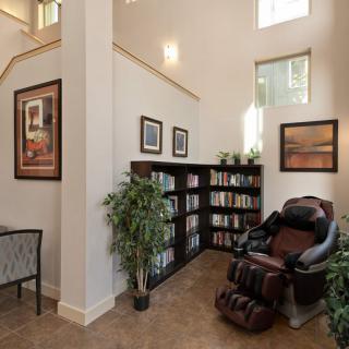 A cozy reading nook with a bookshelf, massage chair, and indoor plants.