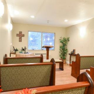 A small chapel with wooden pews, an altar, and a cross on the wall.