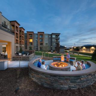 Residents gather around a fire pit in the courtyard of a modern apartment complex during the evening.