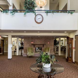A spacious lobby featuring a central clock, chandelier, and seating area surrounded by plants.