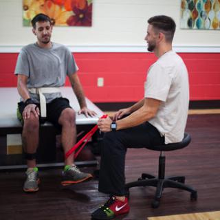 A patient engages in a physical therapy session with a therapist using resistance bands.
