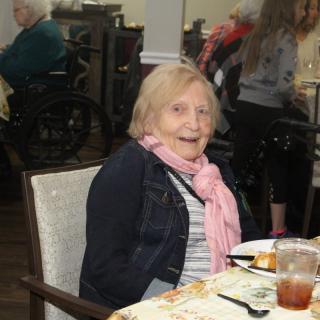 An elderly woman enjoying a meal at a dining table indoors.
