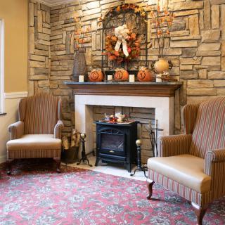 A cozy living room with a stone fireplace, decorated with autumn-themed ornaments and two armchairs.