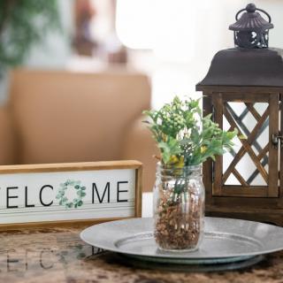 A cozy arrangement featuring a welcome sign, lantern, and small plant on a tray.