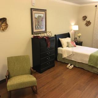 A cozy bedroom with a single bed, green chair, and wooden flooring.
