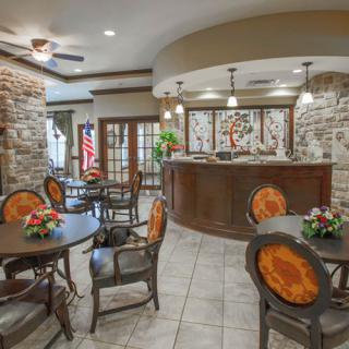 A cozy reception area with stone walls, circular wooden tables and chairs, and warm lighting.