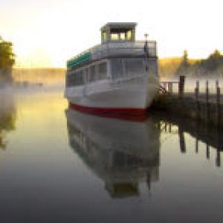 A boat docked on a calm, misty morning with its reflection visible in the water.