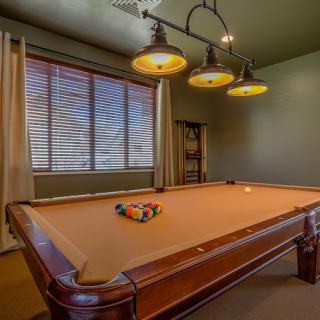 A cozy game room featuring a pool table with overhead lighting and window blinds.