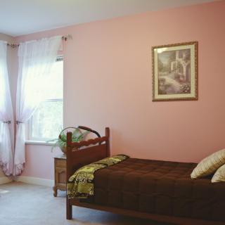 A cozy bedroom with a single bed and pink walls, featuring soft lighting and decorative elements.