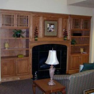 A cozy living room with a wooden fireplace and built-in bookshelves.