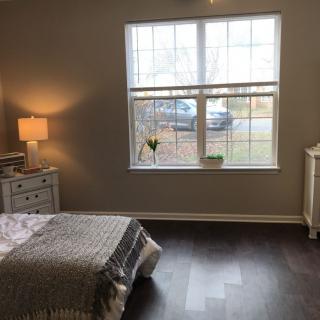 A cozy bedroom featuring a neatly made bed, soft lighting from a bedside lamp, and a large window overlooking the outside.