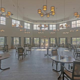 An empty dining room with tables, chairs, and large windows under decorative chandeliers.