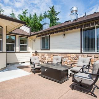 A cozy patio with outdoor seating and a table, set against the backdrop of a modern house exterior on a sunny day.