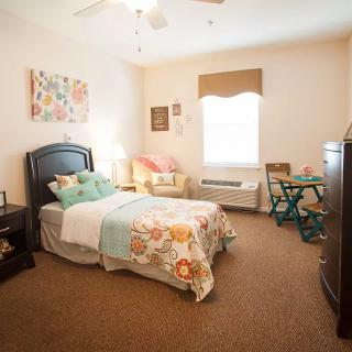 A cozy bedroom with a single bed featuring colorful bedding, a comfortable chair, and a small table near the window.