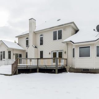A two-story house with a wooden deck covered in snow during winter.