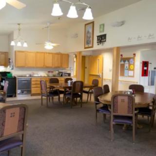 A spacious community kitchen and dining area with wooden cabinets, tables, and chairs.
